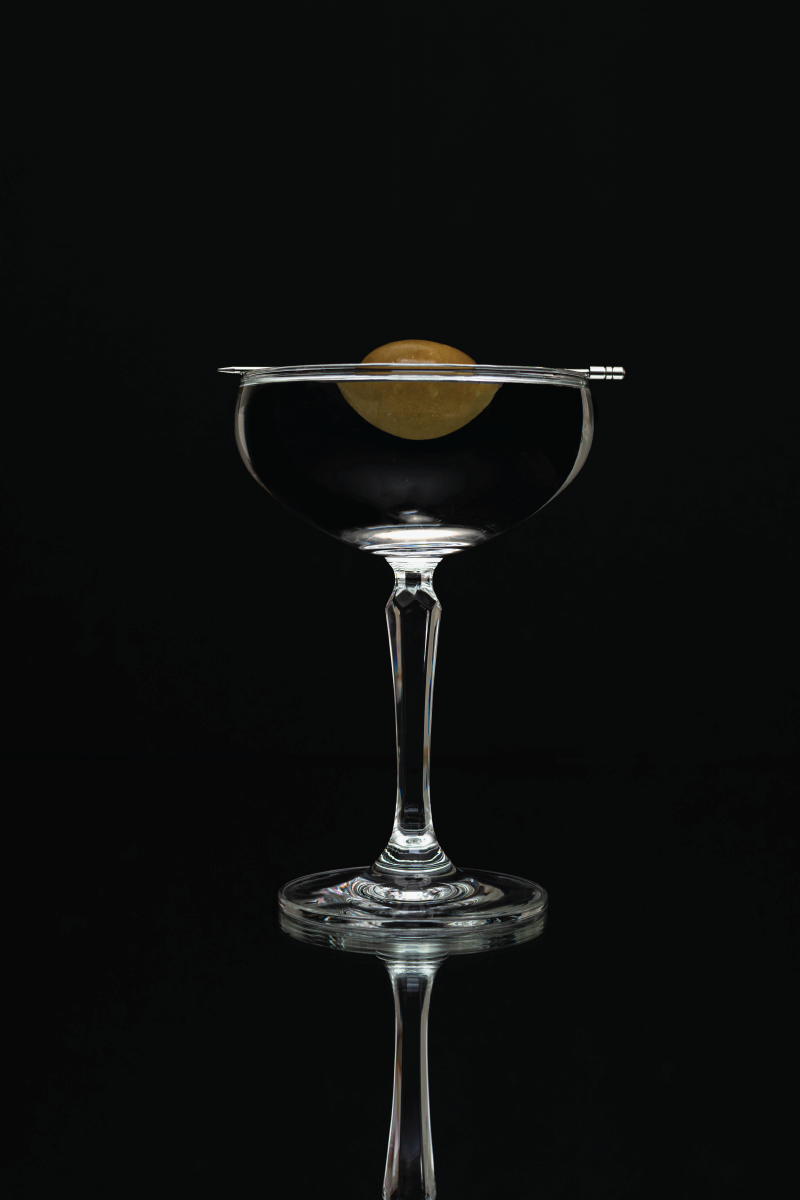 A reflective shot of a martini with a large olive