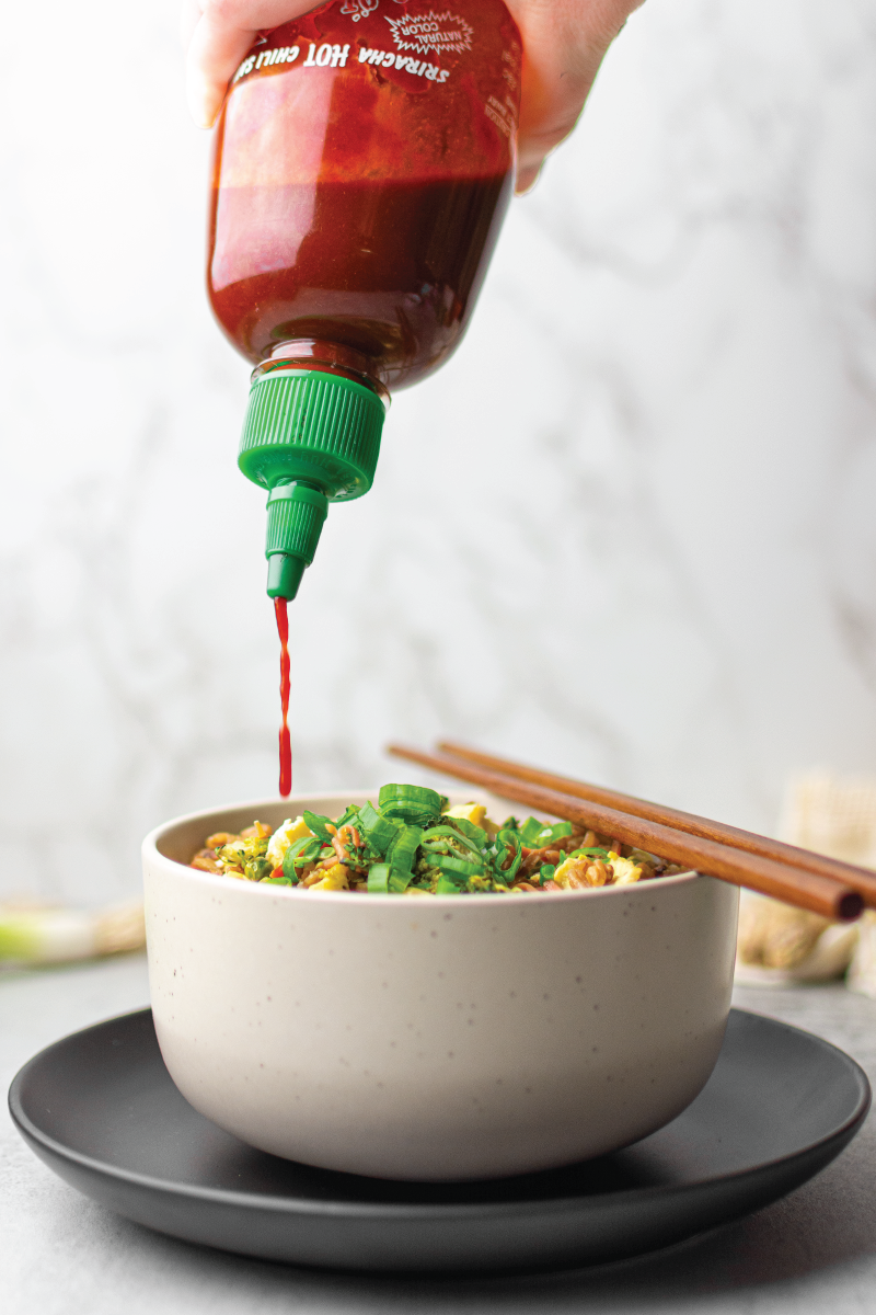 sriracha hot chili sauce pouring on farro fried rice