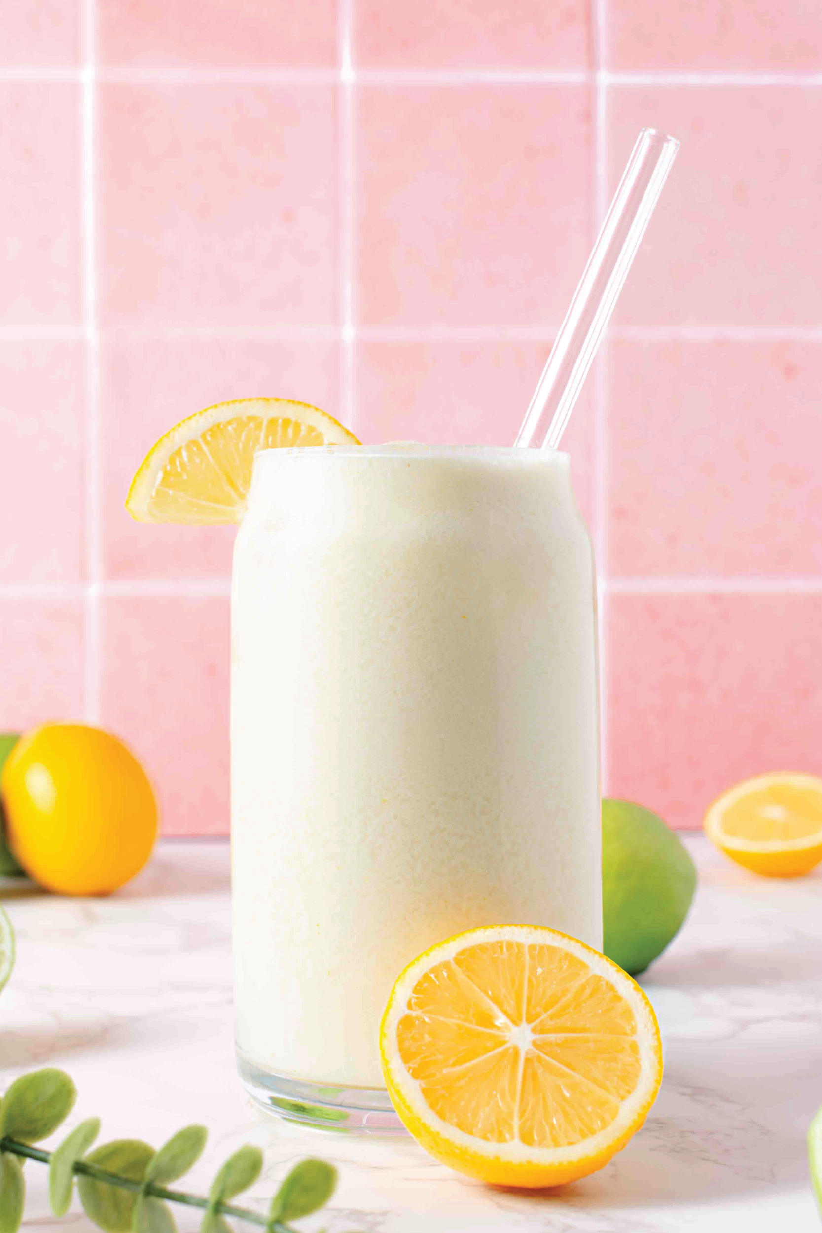 a lemonade mocktail in front of a pink tile background with lemons and limes